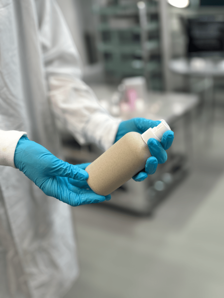 a person wearing lab gloves holding an unlabeled bottle of cosmetic in a clean room environment