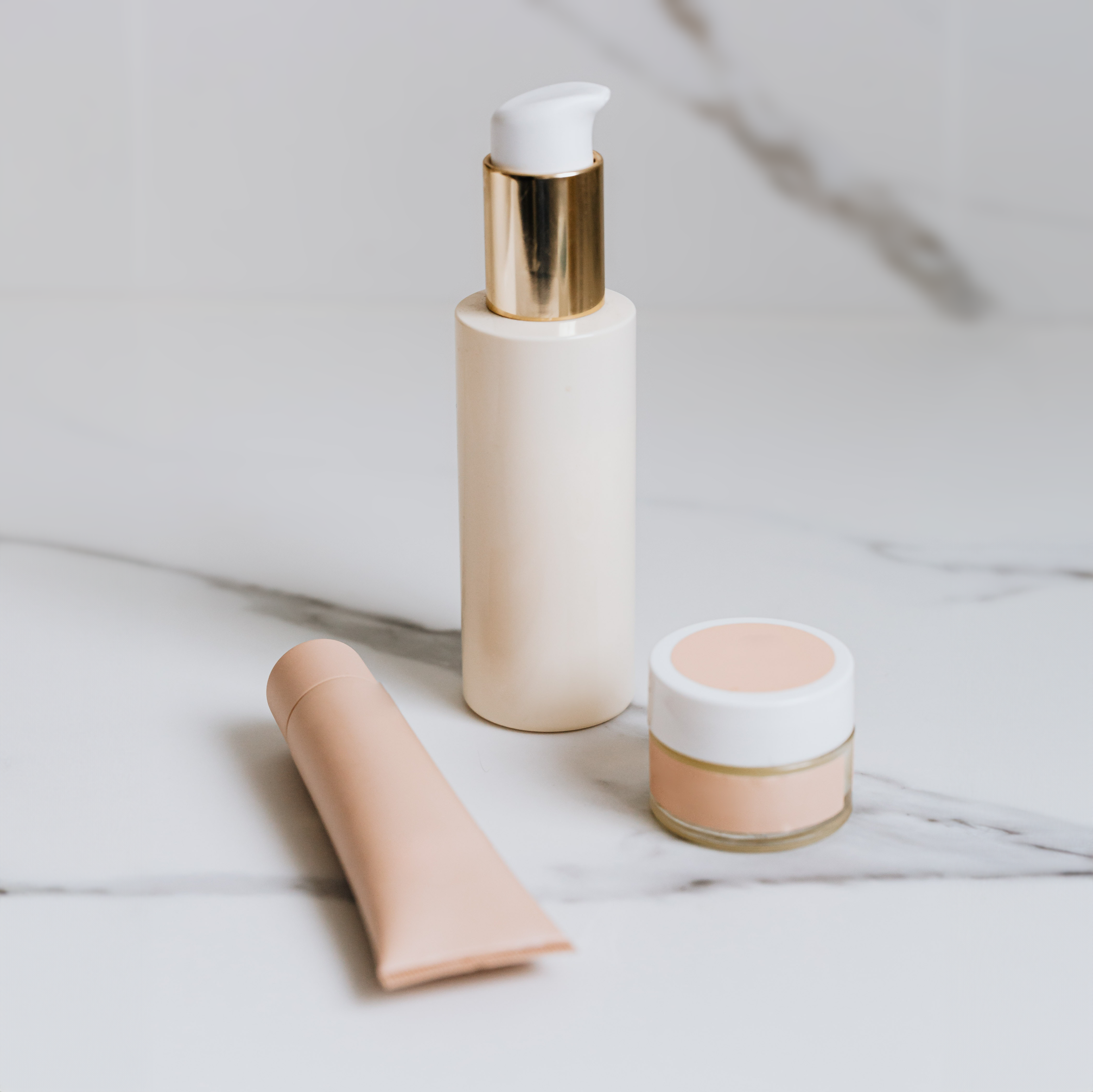 a bottle a tube and a jar of skincare products on a marble surface